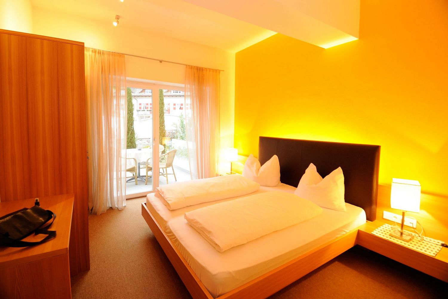 Ein gemütliches Hotelzimmer mit einem Doppelbett, warmen gelben Wandfarben und einer Terrassentür, die nach draußen führt.
