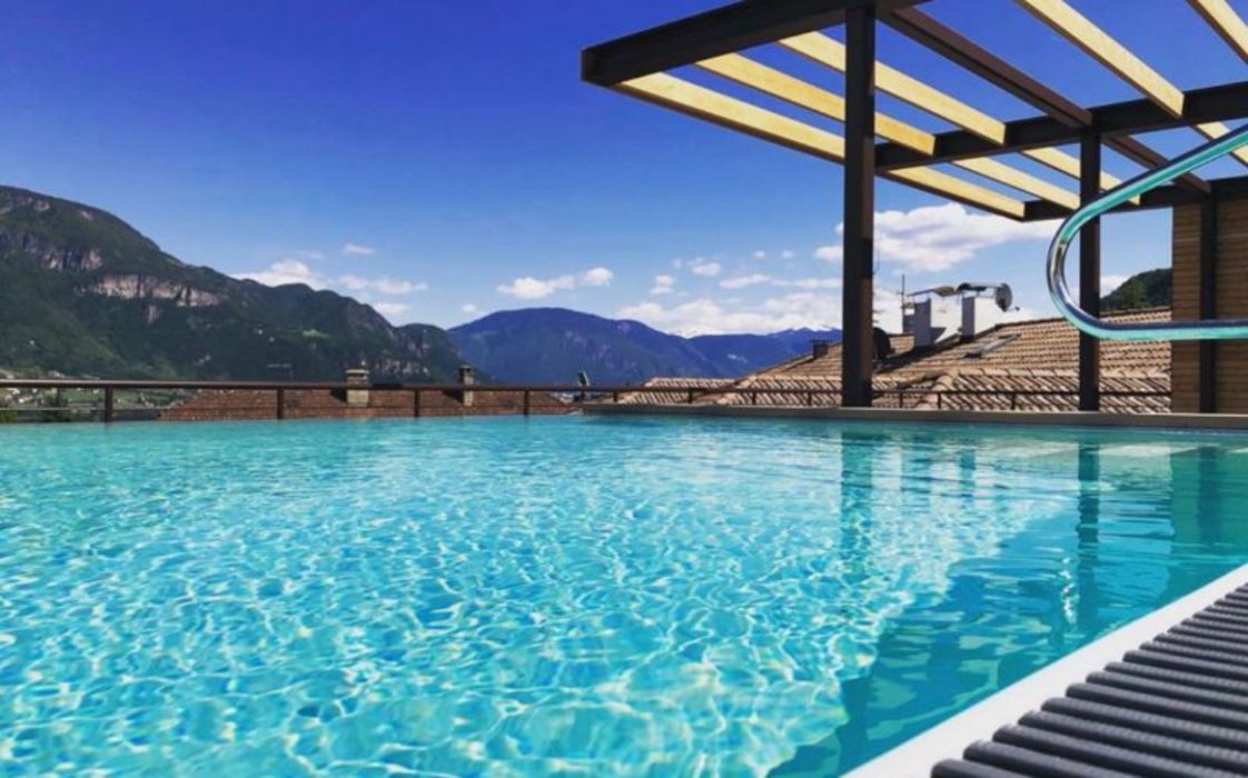 Ein Infinity-Pool auf einer Dachterrasse mit Blick auf Gebirgsketten unter einem klaren blauen Himmel.