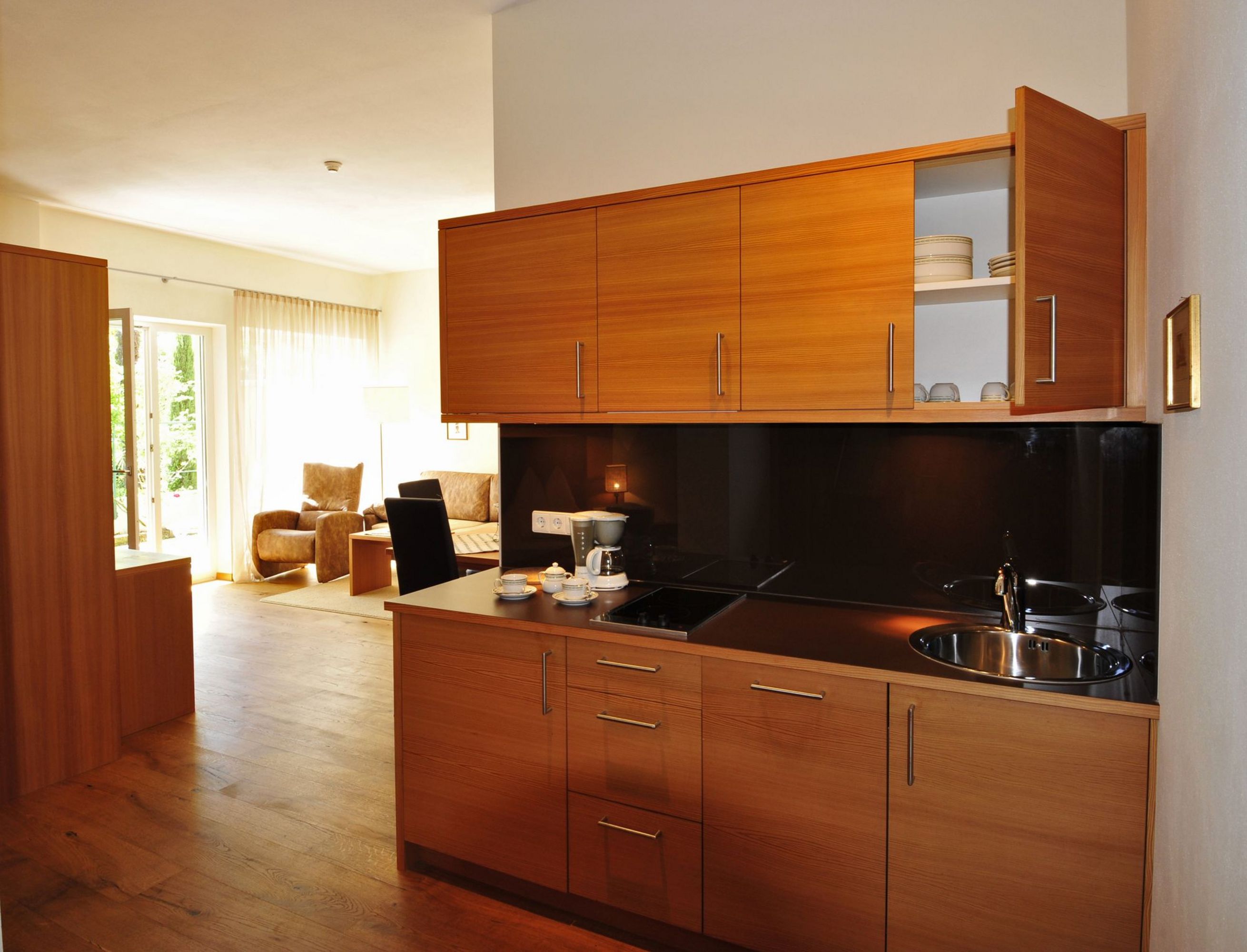Eine Einbauküche aus Holz mit schwarzen Elementen und Spülbecken vor einem hellen Wohnbereich mit Zugang zur Terrasse.