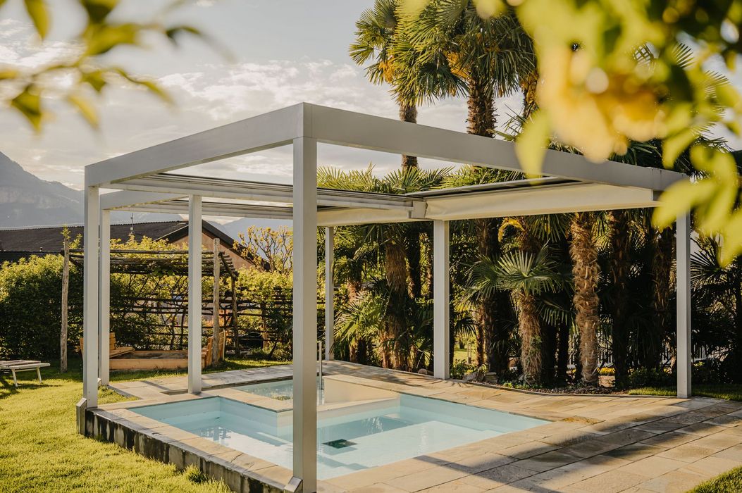 Una piccola piscina esterna quadrata con telaio bianco e copertura in un giardino con palme.