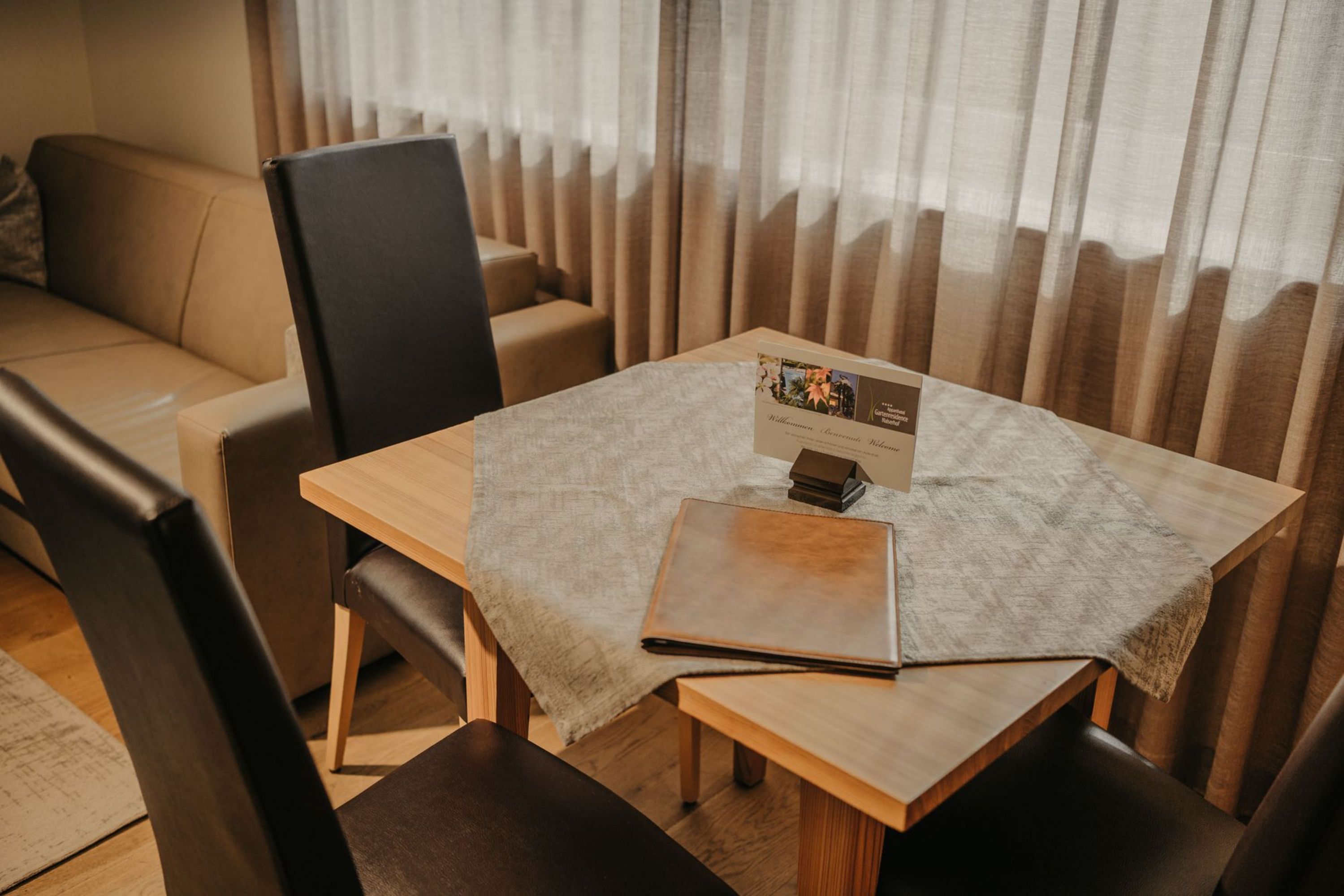 Ein Holztisch mit einer Tischdecke und einem braunen Aufsteller steht vor einem Sofa mit beigen Polstern.