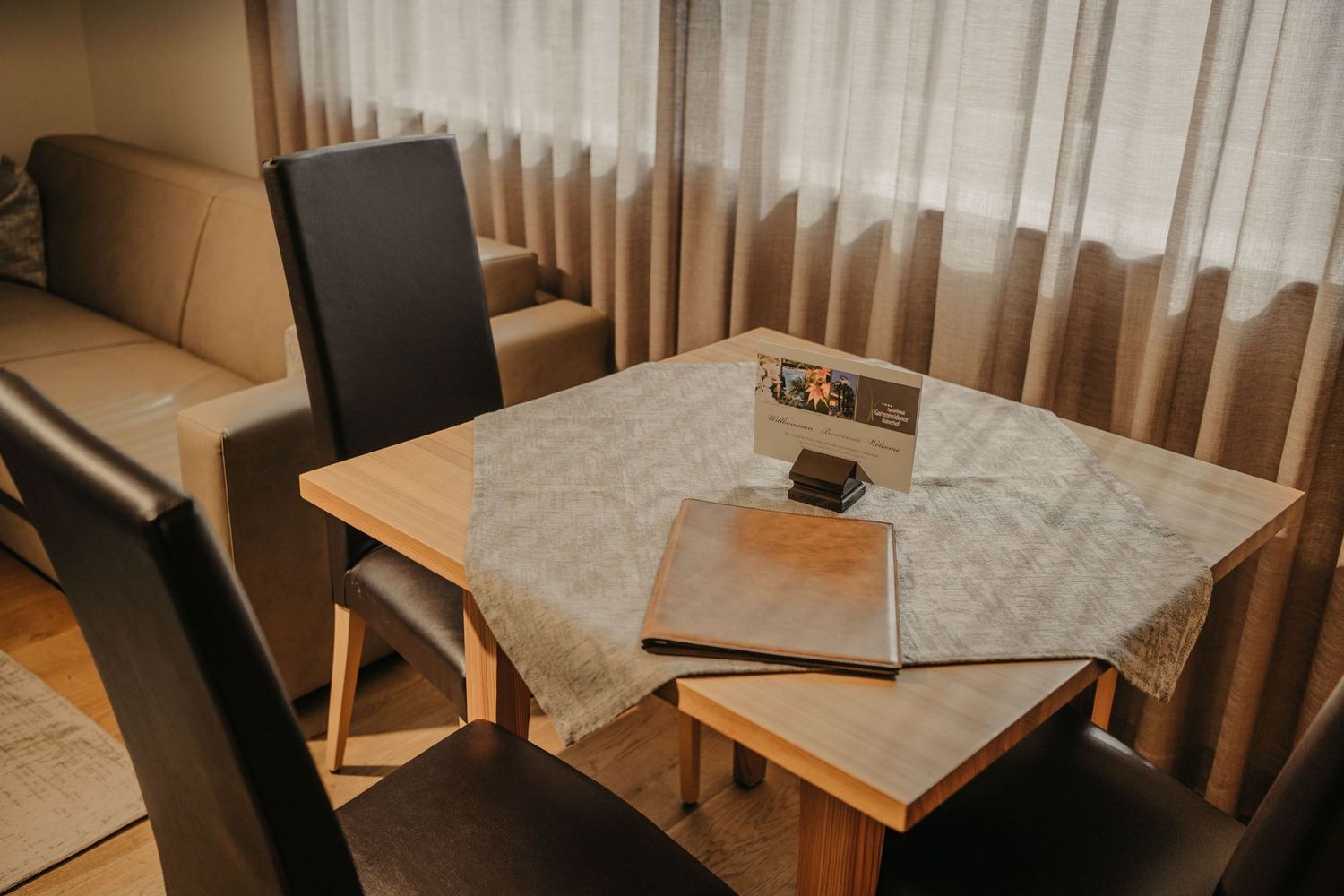Ein Holztisch mit einer Tischdecke und einem braunen Aufsteller steht vor einem Sofa mit beigen Polstern.