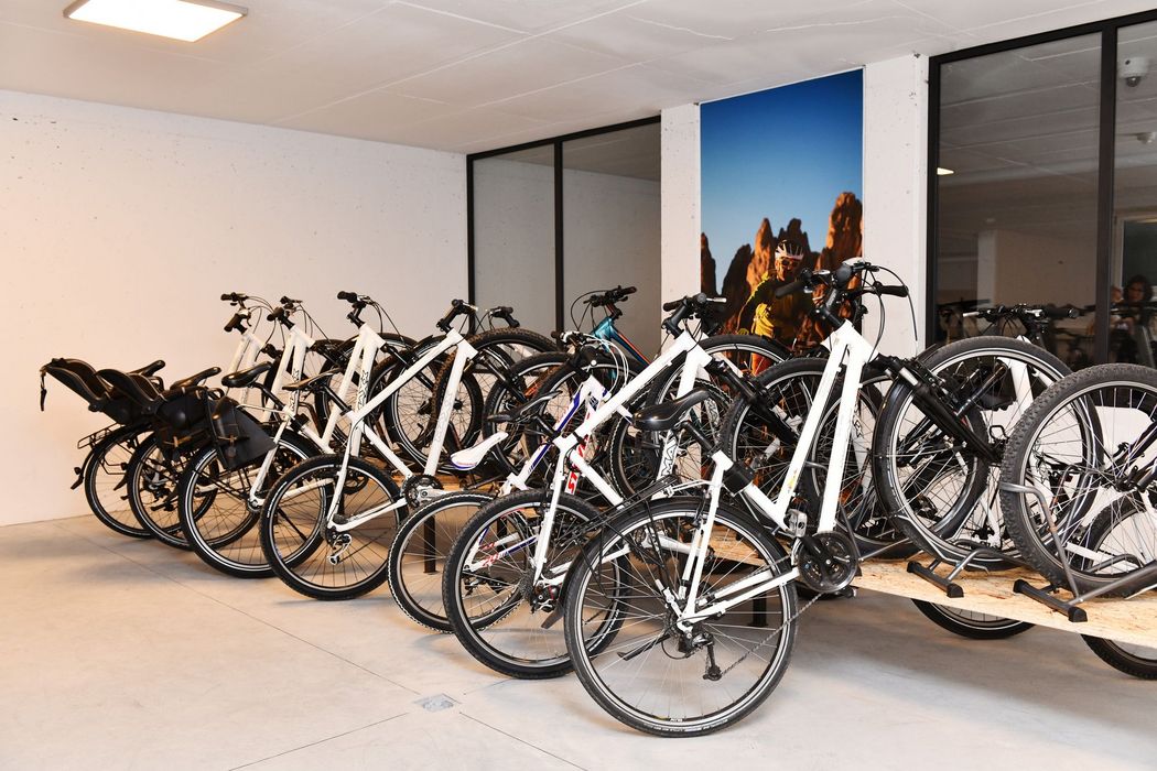 Una fila di biciclette bianche è parcheggiata in una luminosa rimessa o garage, alcune sistemate su una pedana in legno.
