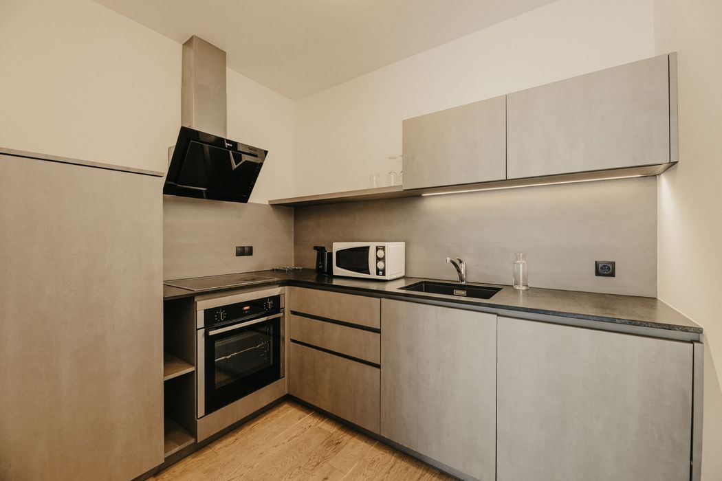 Eine moderne Einbauküche mit grauen Fronten, dunkler Arbeitsplatte, einem Backofen mit Induktionskochfeld, einer Dunstabzugshaube, einer Mikrowelle und einem Spülbecken.