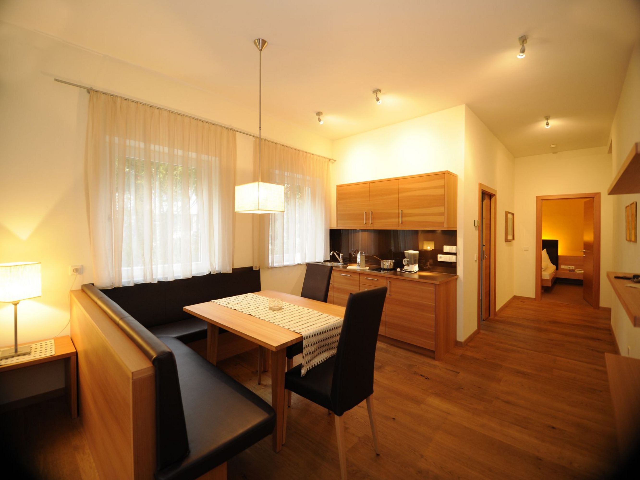 Ein gemütlicher Essbereich mit Holztisch, schwarzer Eckbank und Stühlen neben einer kleinen Küchenzeile.