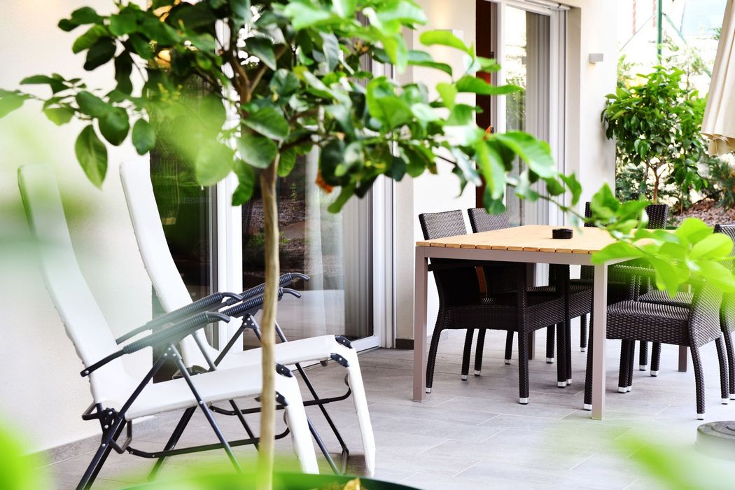 Una terrazza con sedie pieghevoli bianche in primo piano e un tavolo con sedie in vimini scuro sullo sfondo.