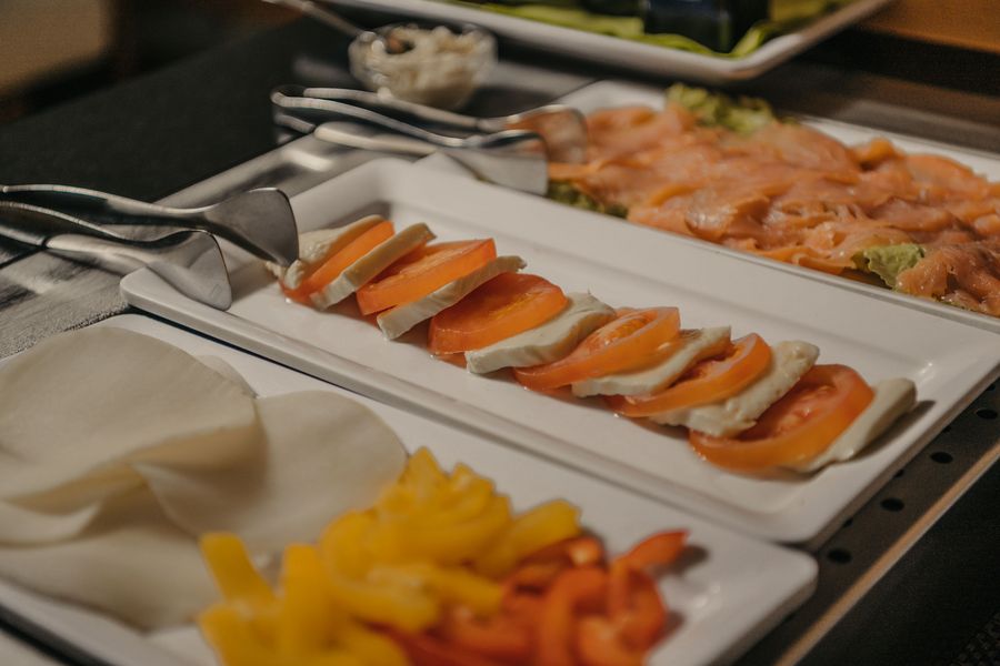 Ein Buffetbereich mit verschiedenen Servierplatten, auf denen Tomaten-Mozzarella-Scheiben, Räucherlachs, Käsescheiben sowie in Streifen geschnittene gelbe und rote Paprika angerichtet sind.