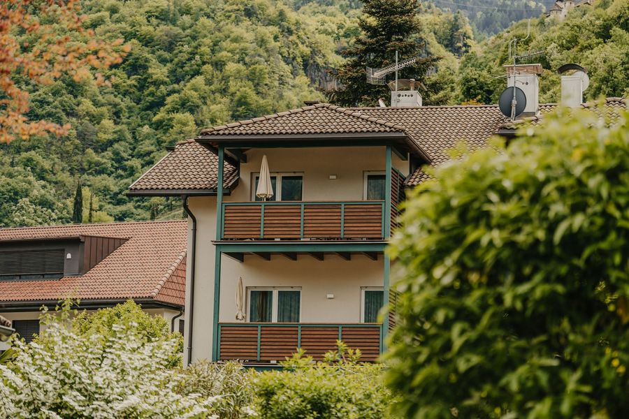 Ein mehrstöckiges Wohnhaus mit Ziegeldach und Balkonen vor einem bewaldeten Berg.