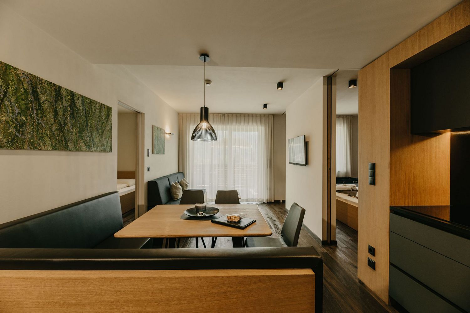 Ein moderner Wohn- und Essbereich mit einer Eckbank, Holztisch, offener Küche und Blick in angrenzende Schlafzimmer.