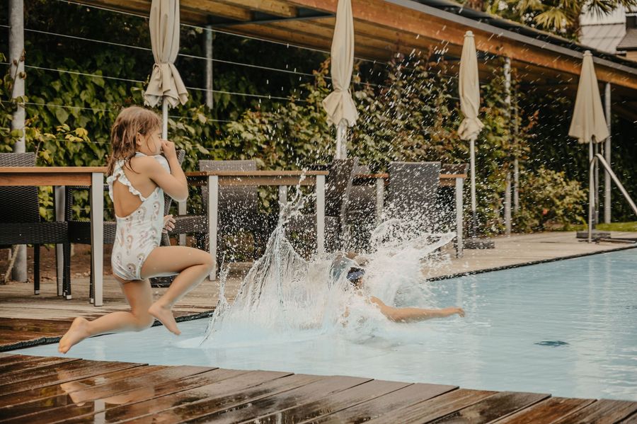 Ein junges Mädchen in einem Badeanzug springt in einen Swimmingpool, während neben ihr Wasser hochspritzt.