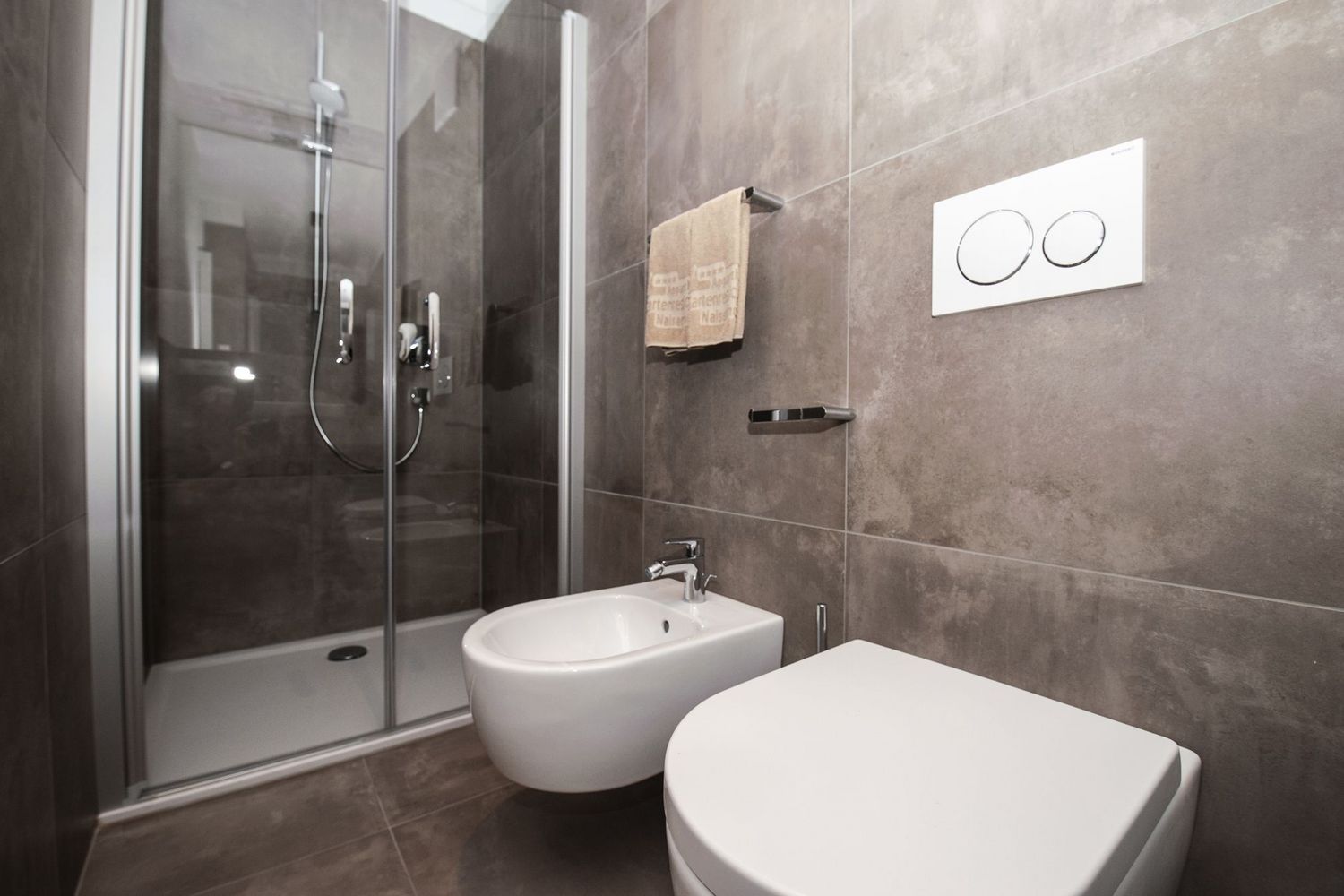 Ein modernes Badezimmer mit einer Glasduschkabine, einem weißen Bidet und einer Toilette vor grauen Fliesenwänden.