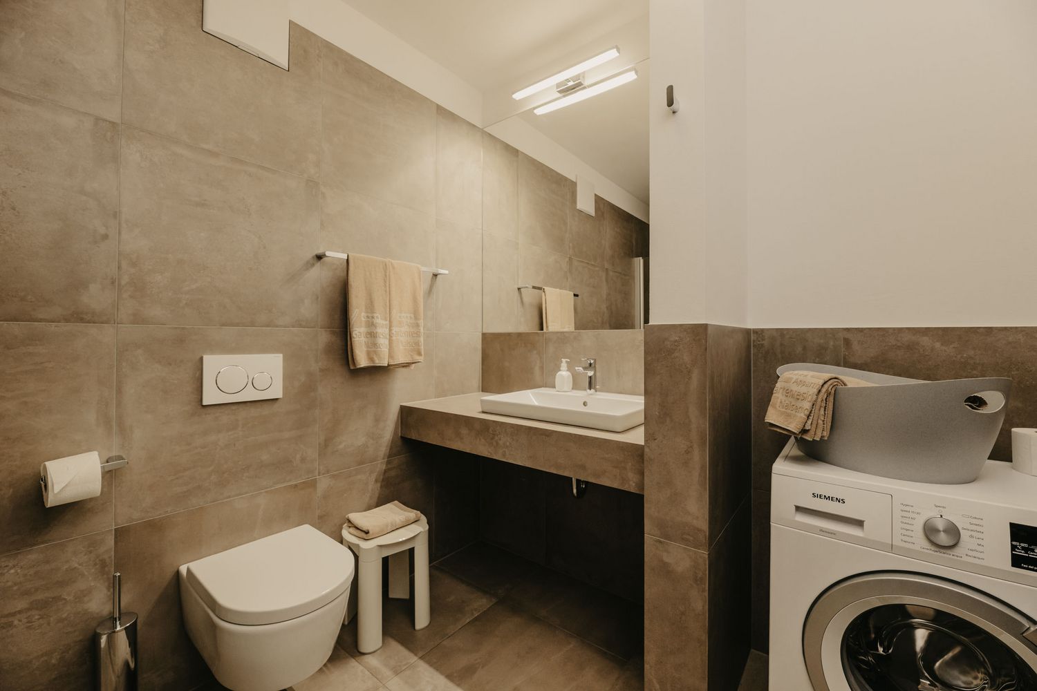 Modernes Badezimmer mit WC, Waschbecken, hängendem Handtuch und einer Waschmaschine mit Wäschekorb.