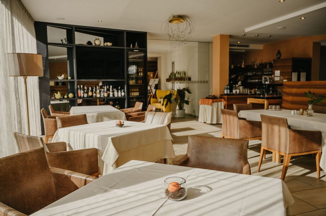 Vista interna di un ristorante raffinato alla luce del giorno con diversi tavoli apparecchiati di bianco e sedie in pelle marrone.