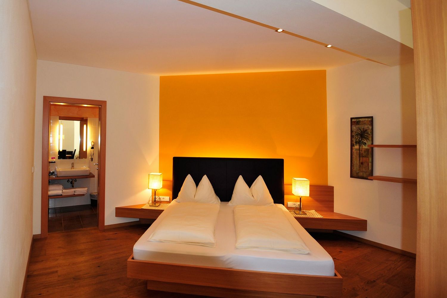 Ein modernes Hotelzimmer mit einem Doppelbett, einer leuchtend orangefarbenen Wand hinter dem Bett und angeschlossenem Badezimmer.